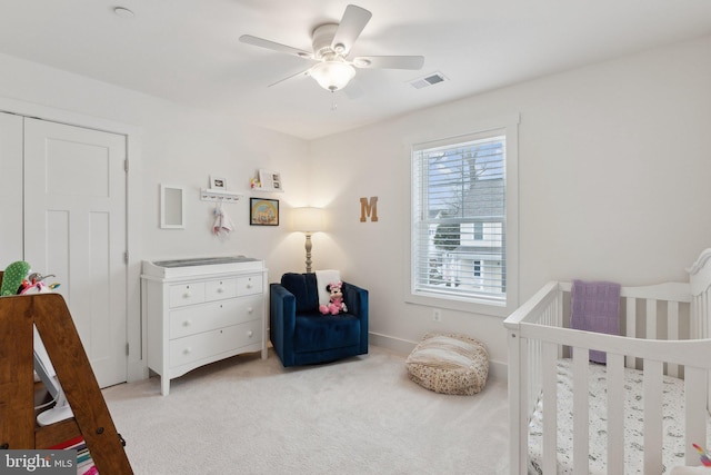 carpeted bedroom with ceiling fan and a crib