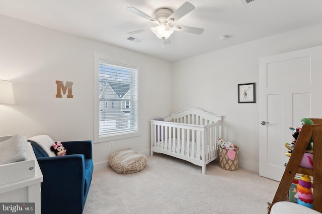 carpeted bedroom featuring ceiling fan and a crib