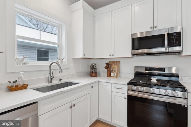 kitchen featuring light stone countertops, sink, stainless steel appliances, and white cabinetry