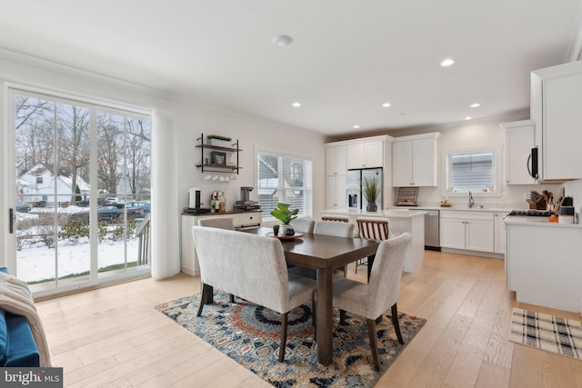 dining space with light wood-type flooring, a wealth of natural light, ornamental molding, and sink