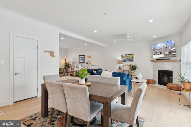 dining room with ceiling fan, a premium fireplace, ornamental molding, and light hardwood / wood-style floors