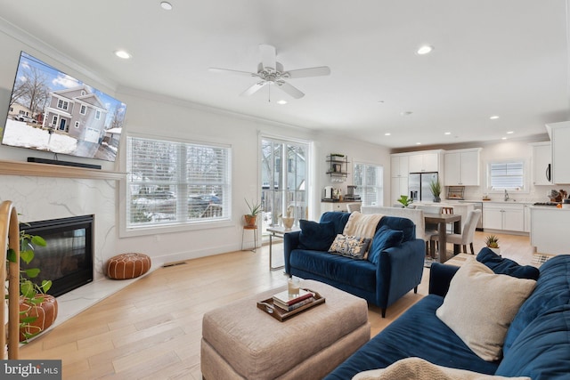 living room featuring ceiling fan, a fireplace, a wealth of natural light, and light hardwood / wood-style floors