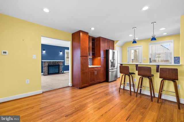 kitchen featuring a fireplace, baseboard heating, stainless steel refrigerator with ice dispenser, a kitchen breakfast bar, and pendant lighting