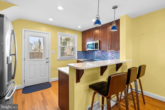 kitchen with appliances with stainless steel finishes, hanging light fixtures, light hardwood / wood-style flooring, a breakfast bar, and backsplash