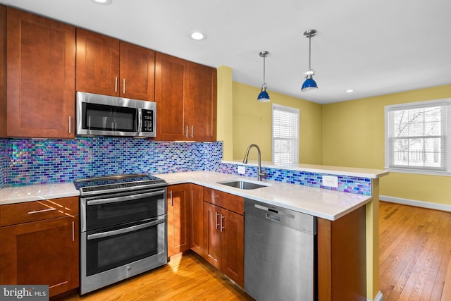 kitchen featuring hanging light fixtures, sink, kitchen peninsula, backsplash, and stainless steel appliances