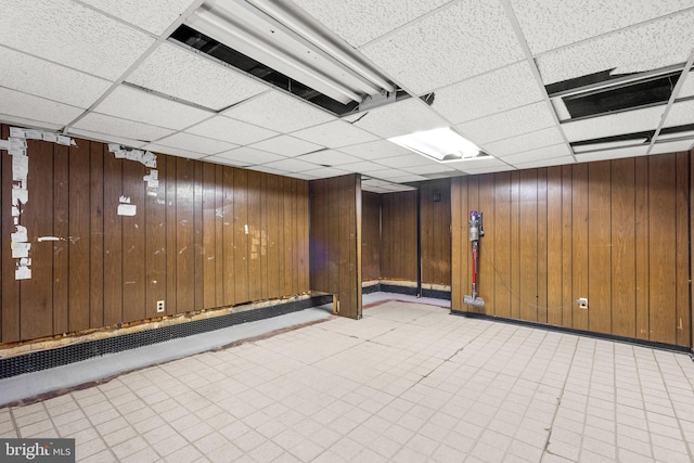 basement with a paneled ceiling and wood walls