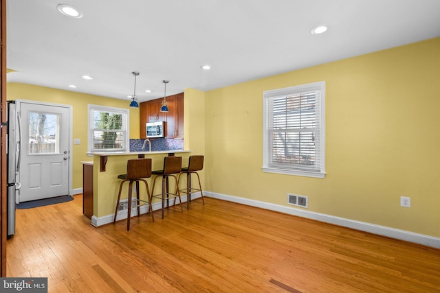 kitchen featuring pendant lighting, backsplash, kitchen peninsula, light wood-type flooring, and a breakfast bar area