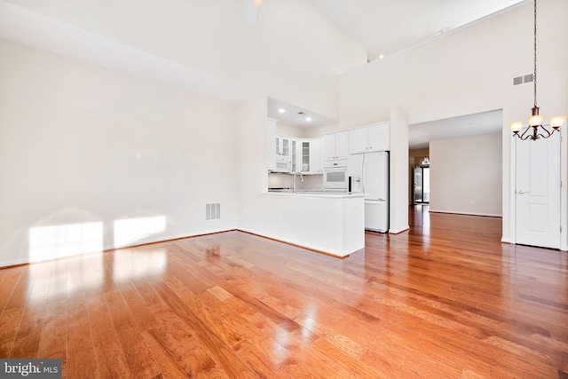 unfurnished living room with sink, light wood-type flooring, a chandelier, and high vaulted ceiling