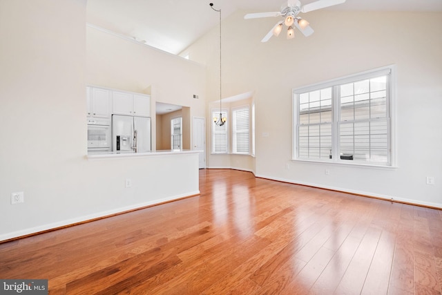 unfurnished living room with ceiling fan with notable chandelier, high vaulted ceiling, and light wood-type flooring