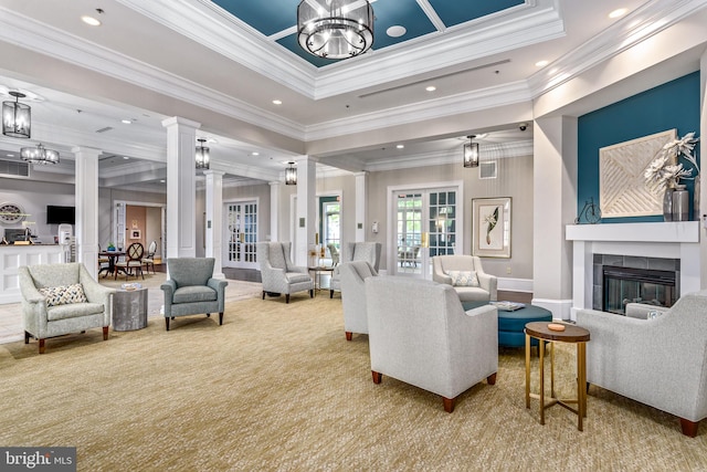 living room with ornate columns, a tiled fireplace, ornamental molding, light colored carpet, and a tray ceiling