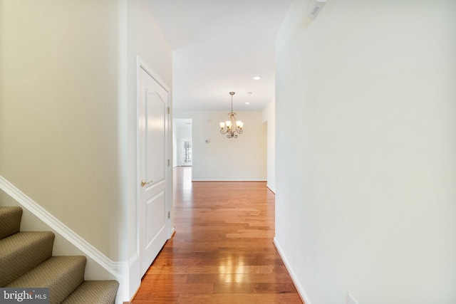 corridor featuring wood-type flooring and an inviting chandelier