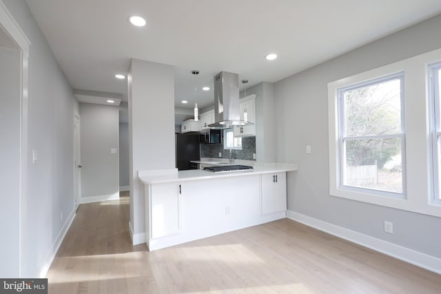 kitchen featuring island exhaust hood, kitchen peninsula, backsplash, black refrigerator, and white cabinets