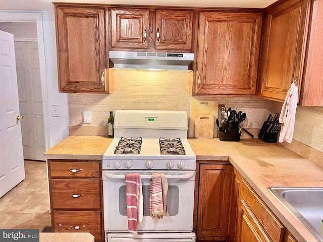 kitchen with decorative backsplash, white range with gas stovetop, sink, and extractor fan