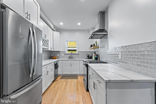 kitchen with sink, stainless steel appliances, light stone countertops, white cabinets, and wall chimney exhaust hood