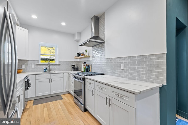 kitchen featuring appliances with stainless steel finishes, sink, white cabinets, wall chimney range hood, and light hardwood / wood-style flooring