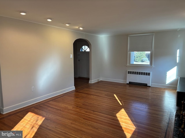 unfurnished living room with radiator, dark wood-type flooring, and ornamental molding