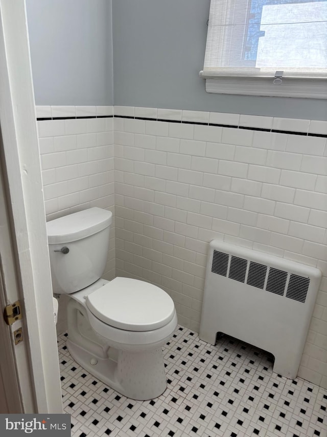 bathroom featuring tile patterned floors, radiator heating unit, tile walls, and toilet