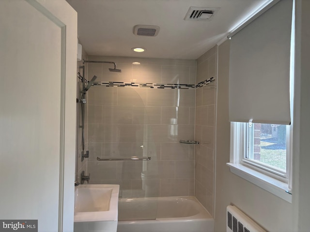 bathroom with tiled shower / bath combo, radiator, and sink