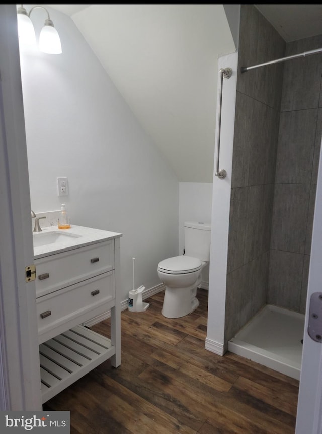 bathroom featuring a tile shower, wood-type flooring, lofted ceiling, toilet, and vanity