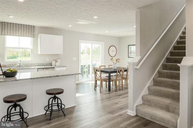 kitchen featuring a kitchen bar, light stone countertops, a healthy amount of sunlight, hardwood / wood-style flooring, and white cabinetry