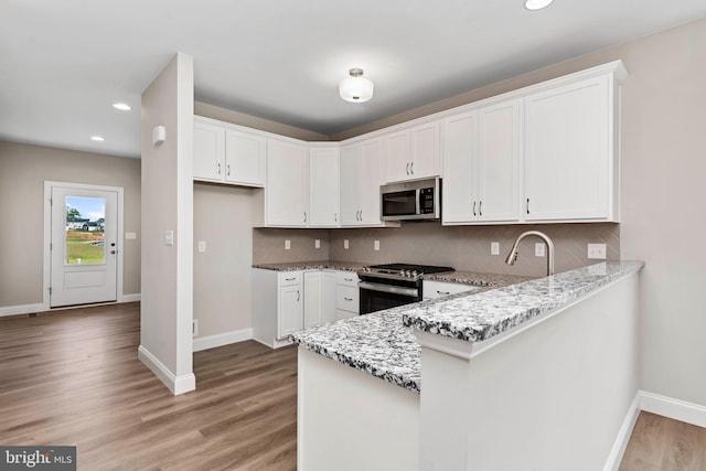 kitchen with stainless steel appliances, light stone countertops, and white cabinets