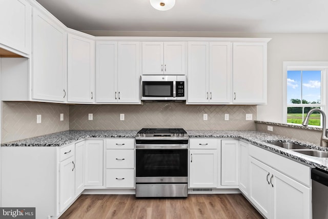 kitchen with sink, light hardwood / wood-style flooring, appliances with stainless steel finishes, white cabinetry, and light stone countertops