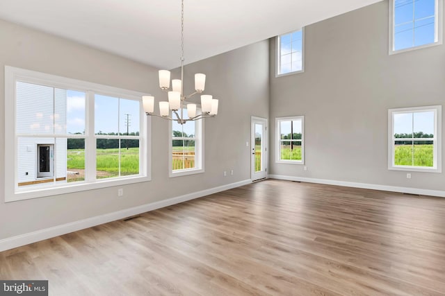 unfurnished dining area featuring a notable chandelier, a towering ceiling, and light hardwood / wood-style flooring