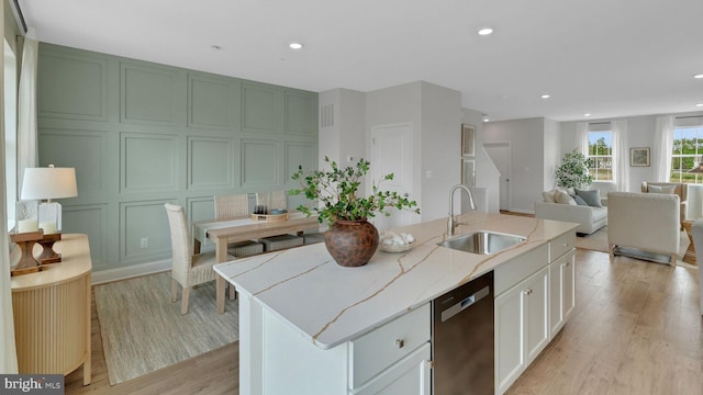 kitchen featuring white cabinetry, sink, light stone counters, stainless steel dishwasher, and a kitchen island with sink