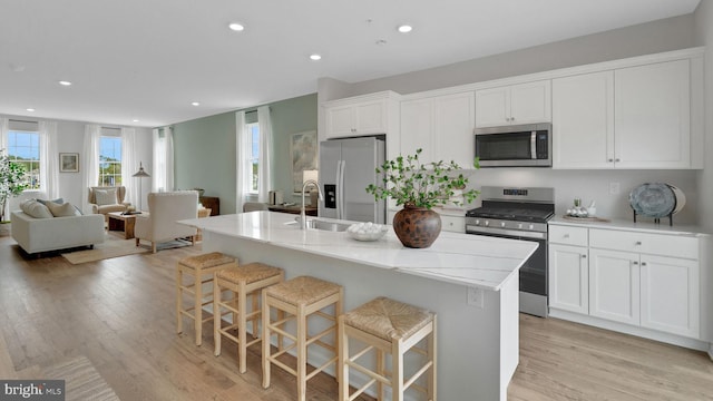 kitchen with a kitchen island with sink, sink, light hardwood / wood-style floors, a kitchen bar, and stainless steel appliances