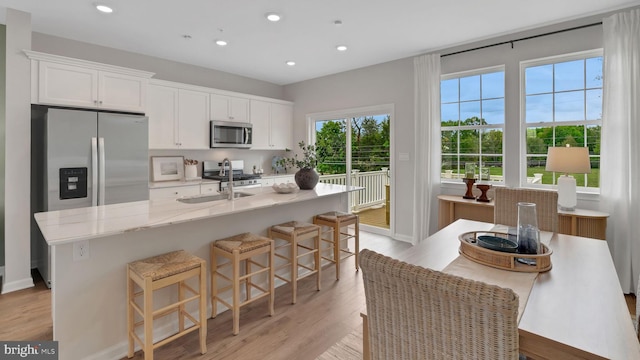 kitchen with a kitchen island with sink, sink, appliances with stainless steel finishes, a kitchen bar, and white cabinetry