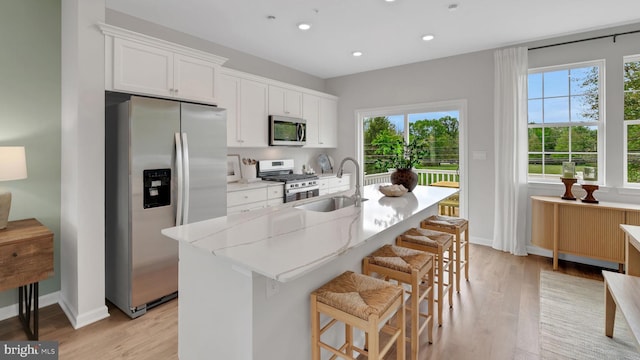 kitchen with stainless steel appliances, a kitchen island with sink, sink, white cabinets, and light hardwood / wood-style floors