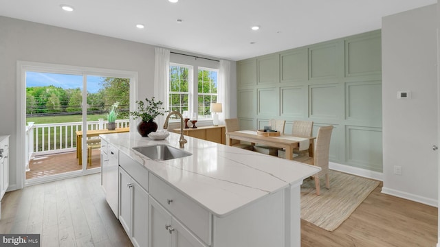 kitchen with a center island with sink, sink, green cabinetry, light hardwood / wood-style flooring, and light stone countertops