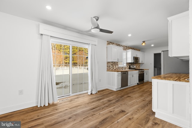 kitchen featuring white cabinetry, ceiling fan, light wood-type flooring, backsplash, and appliances with stainless steel finishes