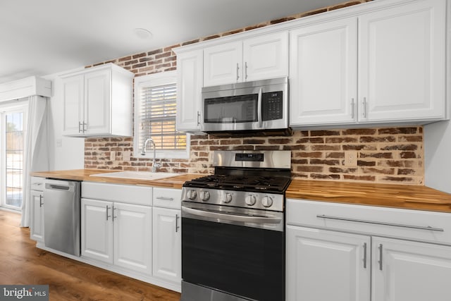 kitchen featuring stainless steel appliances, butcher block counters, white cabinetry, and sink