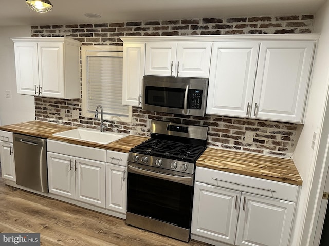 kitchen with stainless steel appliances, brick wall, butcher block counters, white cabinetry, and sink