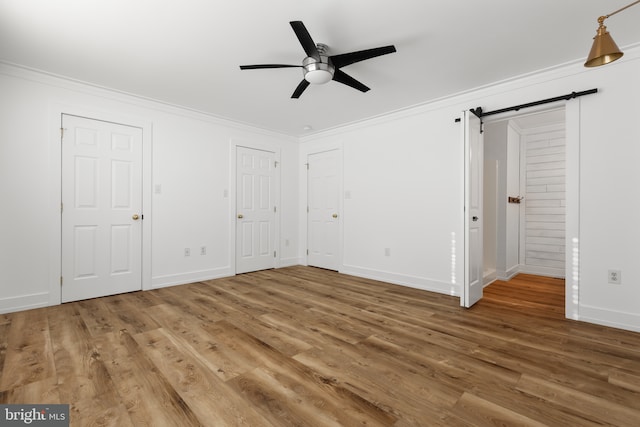 unfurnished bedroom with ceiling fan, a barn door, crown molding, and wood-type flooring