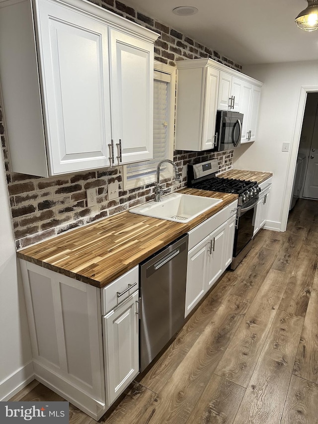 kitchen featuring sink, white cabinetry, hardwood / wood-style floors, brick wall, and appliances with stainless steel finishes