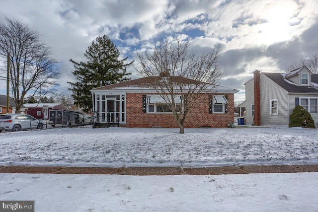 snow covered rear of property featuring central AC unit and a sunroom