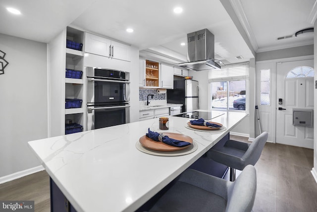 kitchen with white cabinetry, island range hood, appliances with stainless steel finishes, a kitchen breakfast bar, and dark hardwood / wood-style flooring