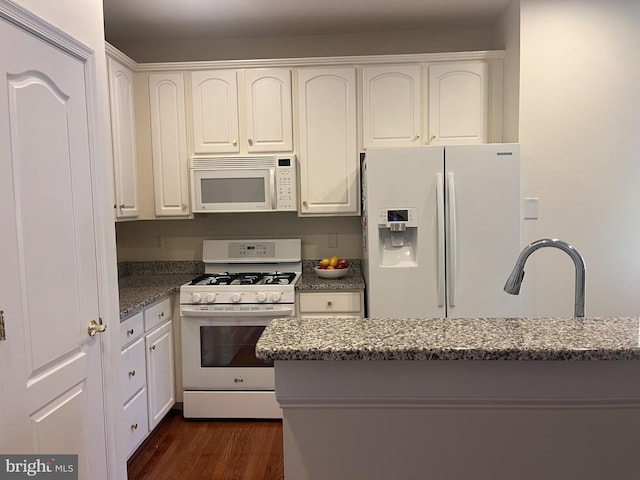 kitchen with white appliances, dark stone counters, and white cabinets