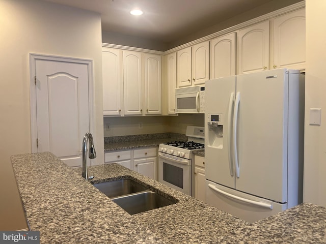 kitchen featuring white cabinetry, sink, white appliances, and dark stone counters