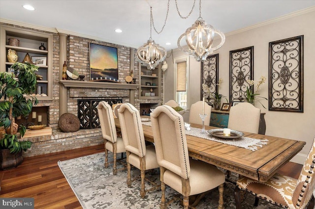 dining room featuring a brick fireplace, ornamental molding, built in shelves, a chandelier, and dark hardwood / wood-style floors