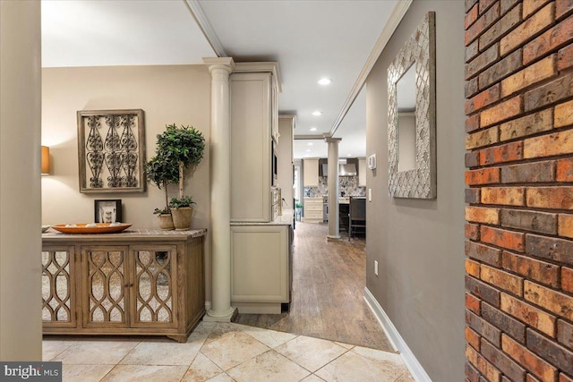 hall with decorative columns, crown molding, and brick wall