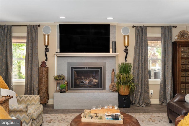 living room with hardwood / wood-style floors, a brick fireplace, a healthy amount of sunlight, and crown molding