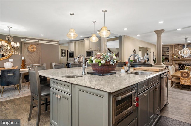 kitchen featuring ornate columns, light stone countertops, sink, a breakfast bar area, and a kitchen island with sink