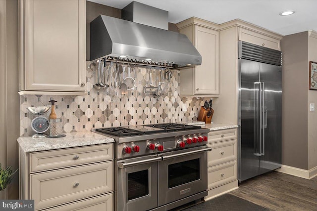 kitchen featuring backsplash, light stone counters, wall chimney exhaust hood, high end appliances, and cream cabinets