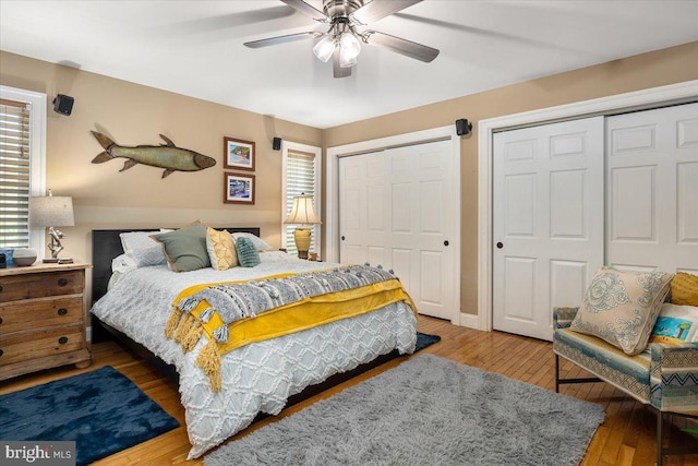 bedroom with hardwood / wood-style floors, ceiling fan, multiple windows, and two closets