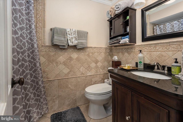 bathroom featuring tile patterned floors, crown molding, toilet, vanity, and tile walls