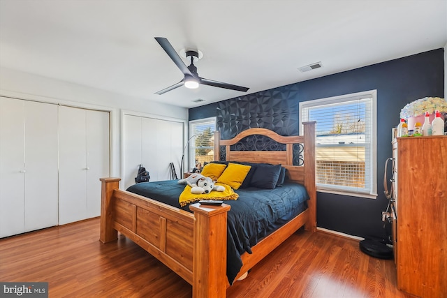 bedroom featuring ceiling fan, dark wood-type flooring, multiple closets, and multiple windows