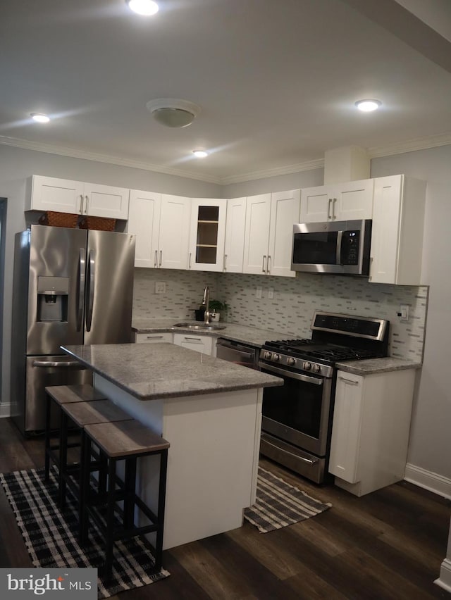 kitchen featuring a breakfast bar, stainless steel appliances, sink, white cabinets, and a center island